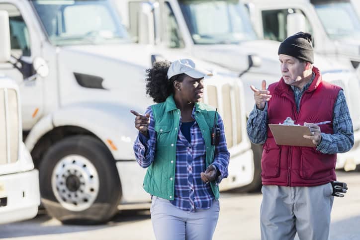 a female trucker and a male holding a clipboard checklist