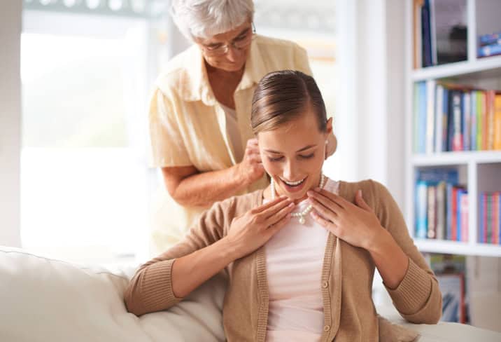 an older woman places an antique necklace on her daughter